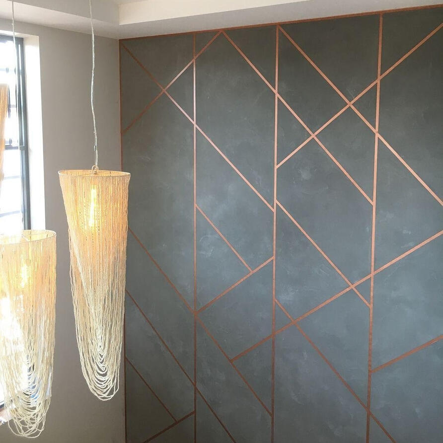 "Interior wall with a modern geometric design in gray with copper lines, featuring two hanging pendant lights with intricate, delicate string designs."